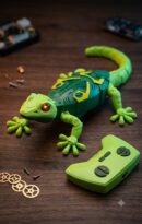 Retail packaging box for the K.LAL Geckos Telecontrol wall-climbing RC toy. The black box displays a bright green robotic gecko with glowing red eyes, alongside text highlighting features like a 2.4 GHz control system, 360-degree spinning on the wall, and an ages 4+ rating.