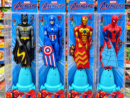 Two images showcasing the flying superhero toy. The first shows a hand pulling a string on a blue launcher to fly a Spider-Man action figure, with an inset highlighting a hidden candy compartment in the base. The second shows four packaged toys in Marvel Avengers boxes, featuring Batman, Captain America, Iron Man, and Spider-Man figures mounted on blue pull-string launchers.