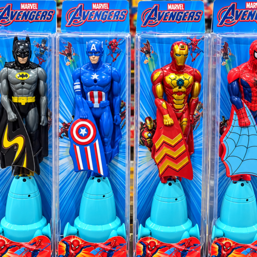 Two images showcasing the flying superhero toy. The first shows a hand pulling a string on a blue launcher to fly a Spider-Man action figure, with an inset highlighting a hidden candy compartment in the base. The second shows four packaged toys in Marvel Avengers boxes, featuring Batman, Captain America, Iron Man, and Spider-Man figures mounted on blue pull-string launchers.