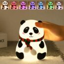 A soft silicone LED night light shaped like a cute panda wearing a red and green striped scarf. A hand is gently pressing down on the squishy panda's head. Along the top, a banner shows the same panda lamp glowing in seven different vibrant colors including warm white, red, purple, blue, and green.