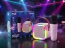 A white MZ S664 Wireless Speaker with a brown carrying strap and an illuminated RGB LED ring, sitting next to a white wireless microphone and its blue retail packaging box in a neon-lit party setting.